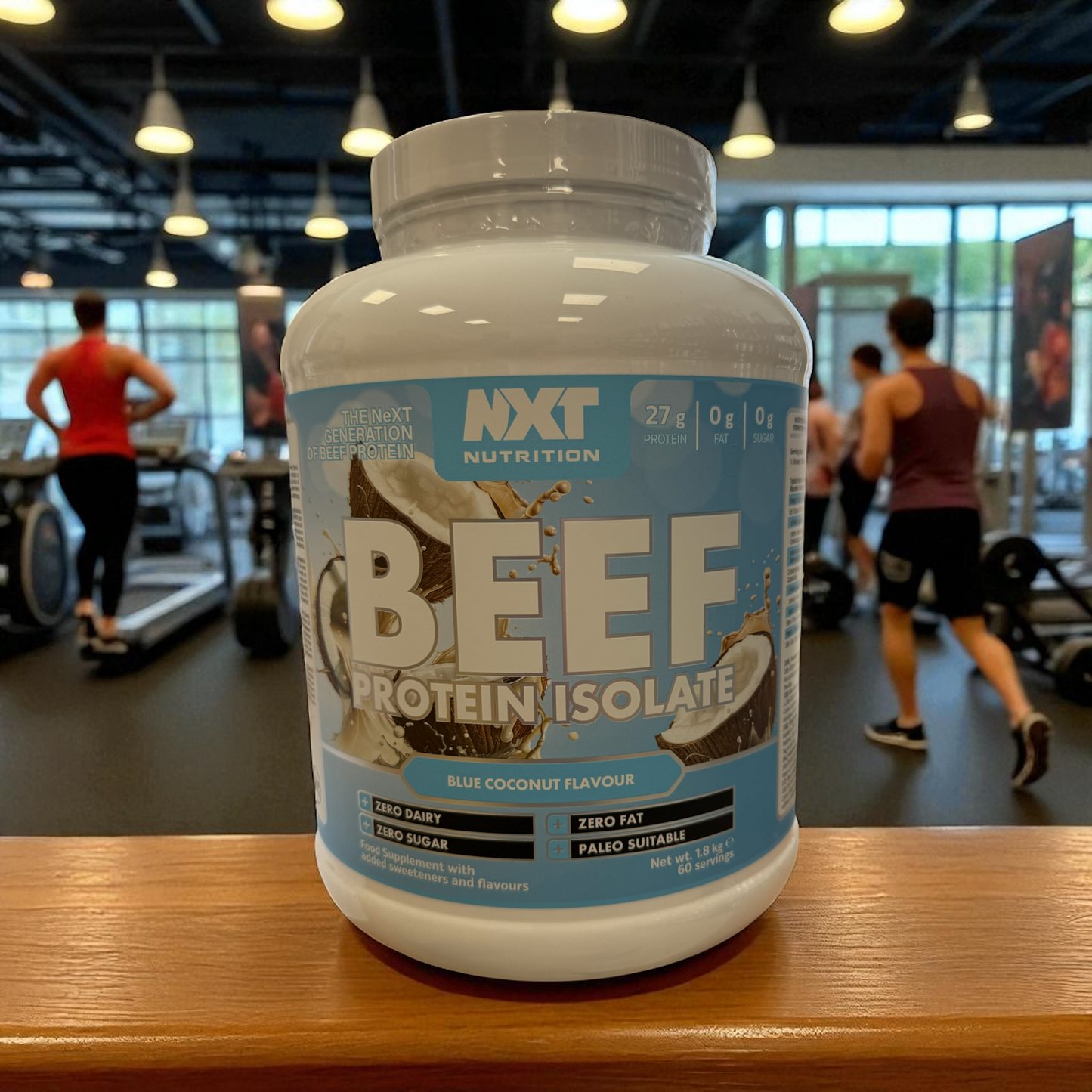 NXT Nutrition Beef Protein Isolate coconut container on a gym counter with people exercising in the background