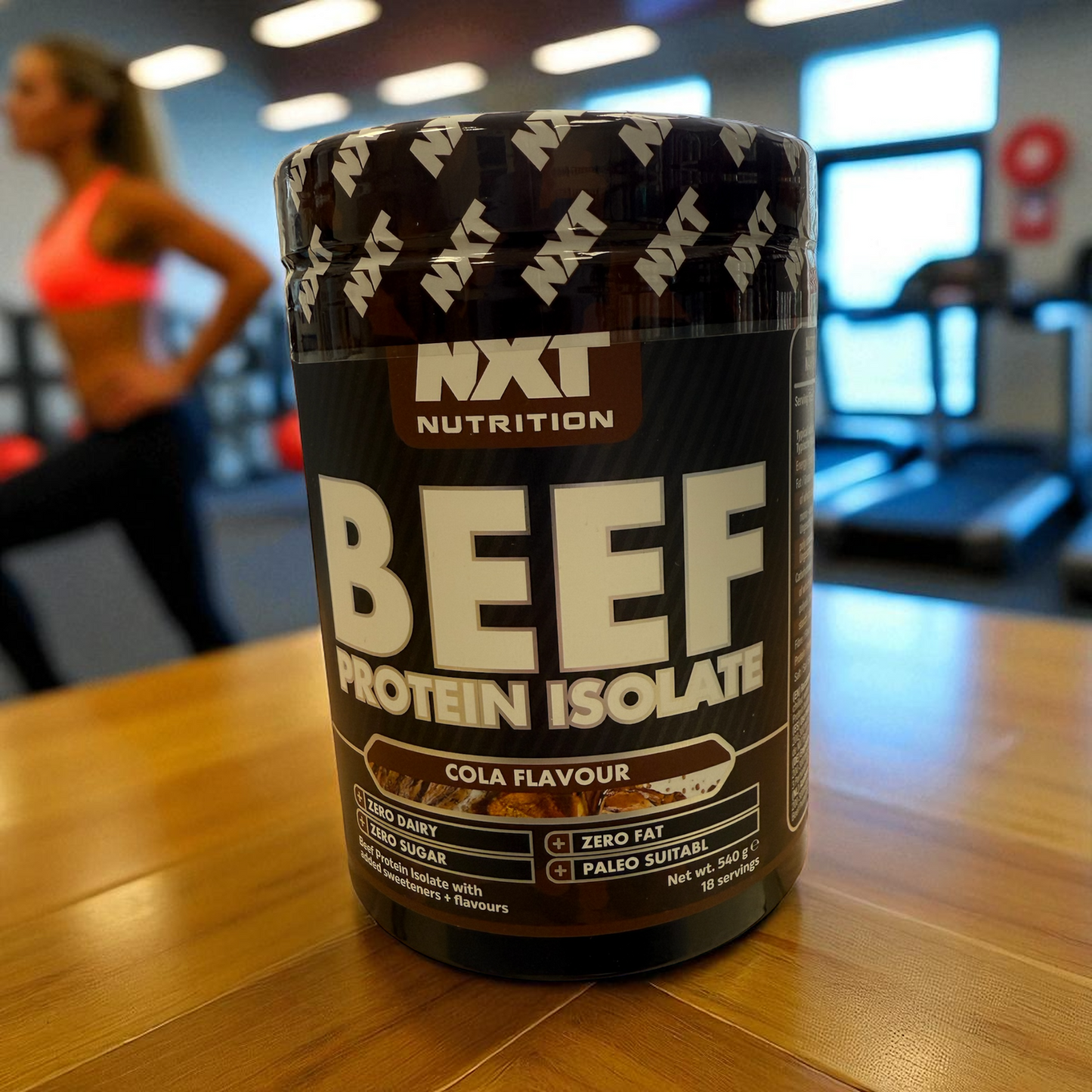 nxt beef isolate tub in Cola flavour sitting on a able in a gym