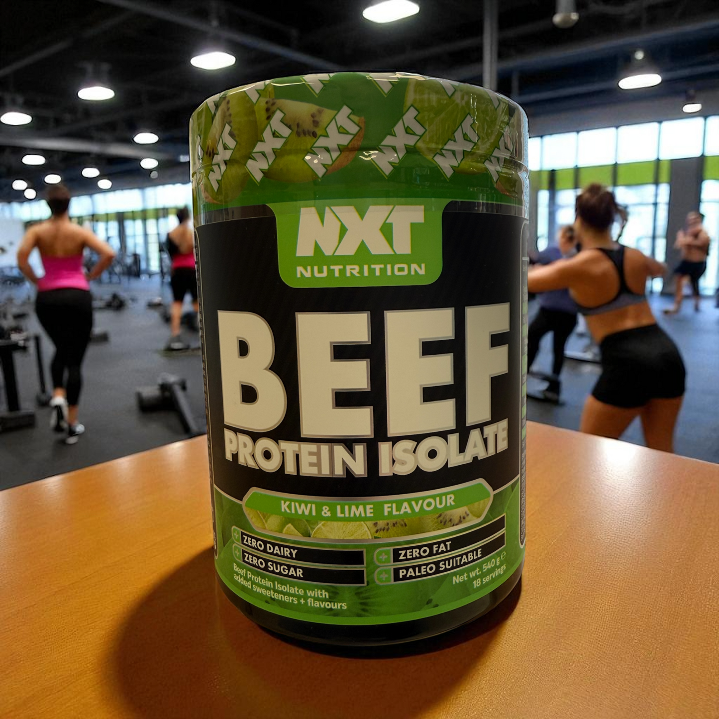 NXT Nutrition Beef Protein Isolate container on a table with people exercising in the background, in kiwi and Lime