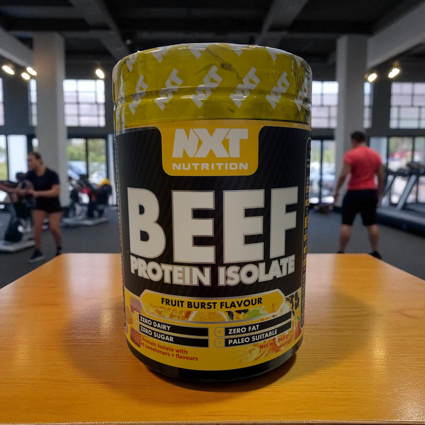 NXT Nutrition Beef Protein Isolate container on a table in a gym setting, in fruit burst flavour