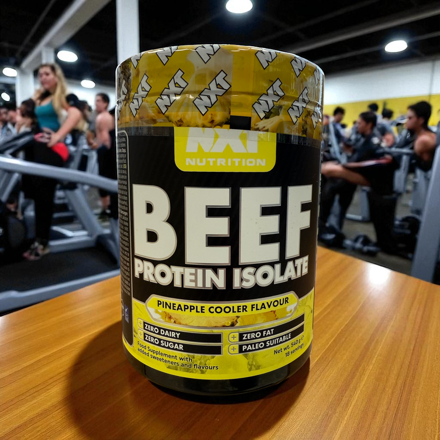 Container of beef protein isolate with a gym in the background in pineapple