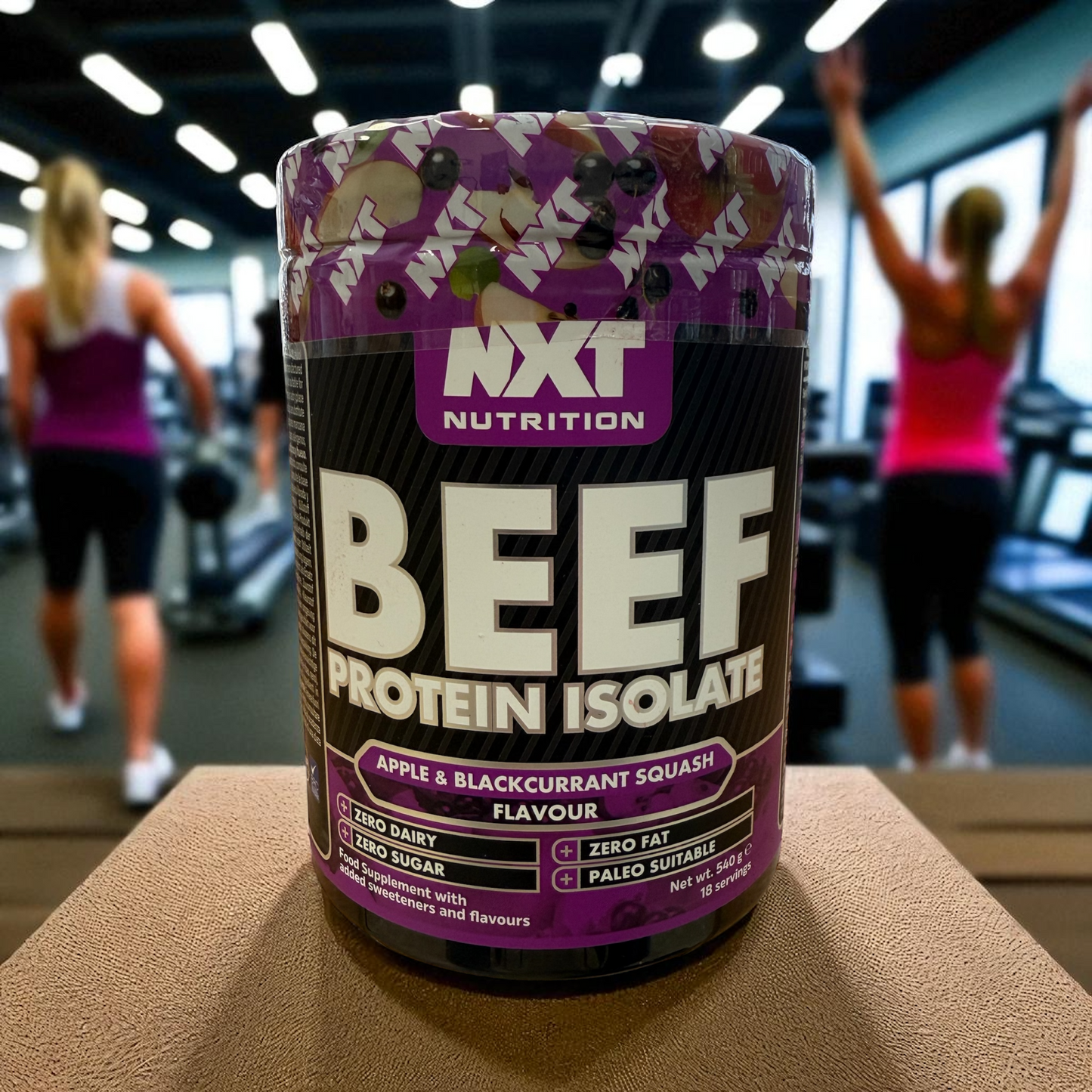 NXT Nutrition Beef Protein Isolate container with people exercising in a gym in the background in apple and blackcurrant flavour