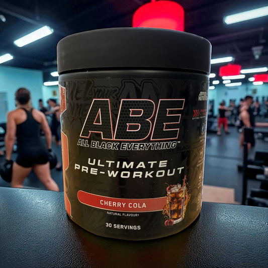 ABE Ultimate Pre-Workout supplement container with cherry cola flavor in a gym setting