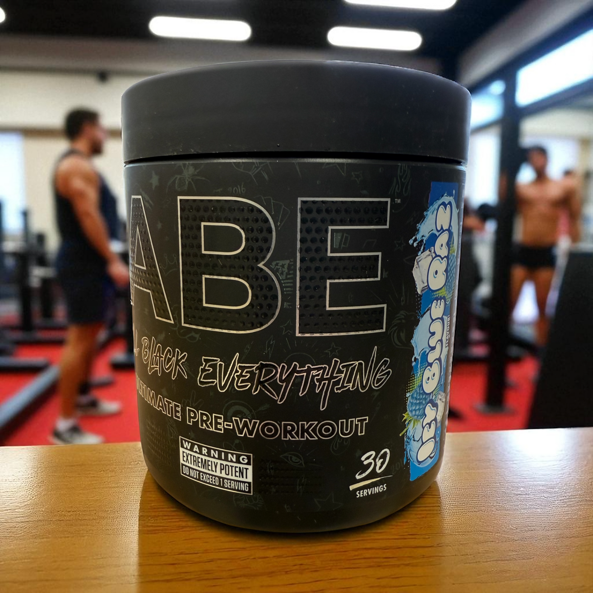ABE Black Everything pre-workout supplement container on a table in a gym setting in Blue Raz flavour
