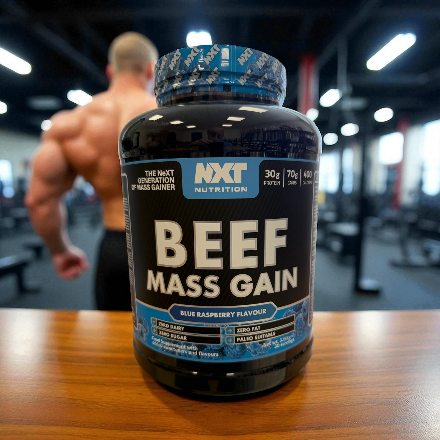 NXT Nutrition Beef Mass Gain supplement bottle on a table with a gym background in Blue Raspberry flavour in a 3kg tub
