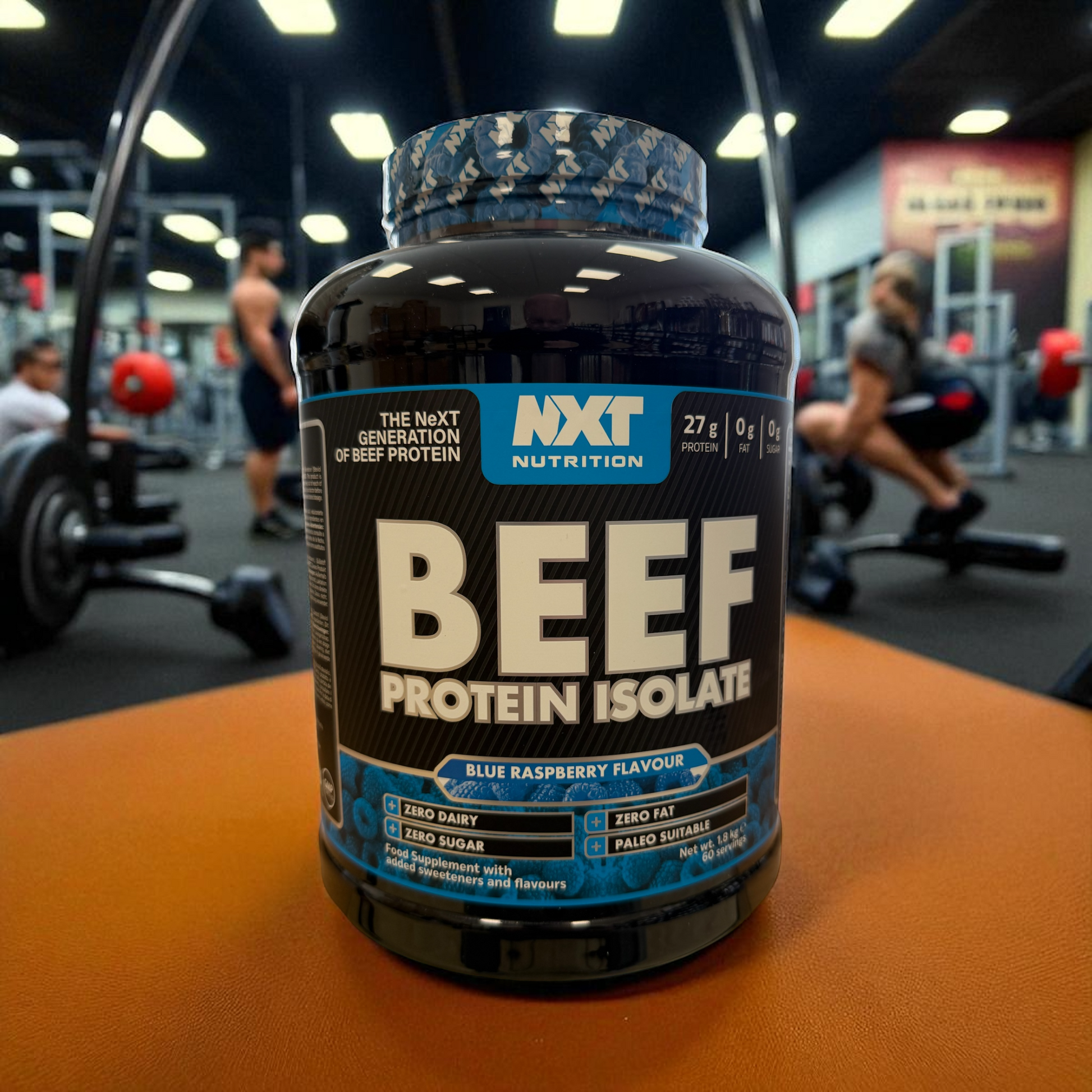 NXT Nutrition Beef Protein Isolate bottle on a table in a gym setting in blue raspberry